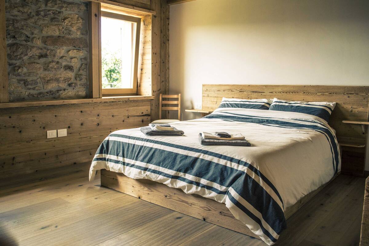 Quarto de cabana de madeira com cama, janela e parede de pedra.