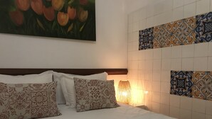 A neatly made bed with patterned pillows, a painting of flowers on the wall, and a tiled wall with decorative patterns. - Old kitchen Cus cus factory Villa with pool and sea view (Funchal)