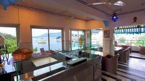 A modern hotel lobby with a glass partition, seating area, and a view of a body of water. - Jheel Hotel and Restaurent (Udaipur)