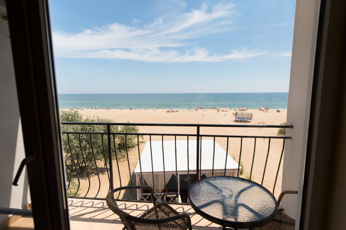 Een balkon met uitzicht op een strand, een tafel en stoelen.