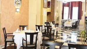 Un comedor de hotel con suelo a cuadros, varias mesas con sillas y una escalera al fondo.