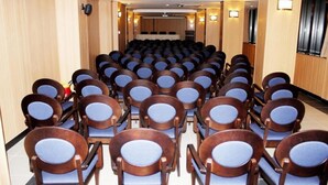 Un salón de conferencias con filas de sillas de madera y un escenario al frente.