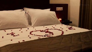 Una habitación de hotel con una cama cubierta de pétalos de rosa dispuestos en forma de corazón.
