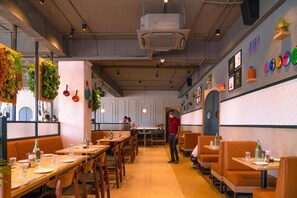 A restaurant interior with booths and tables, a person standing, and wall decorations. - Aloka Stay Inn (Vellore)