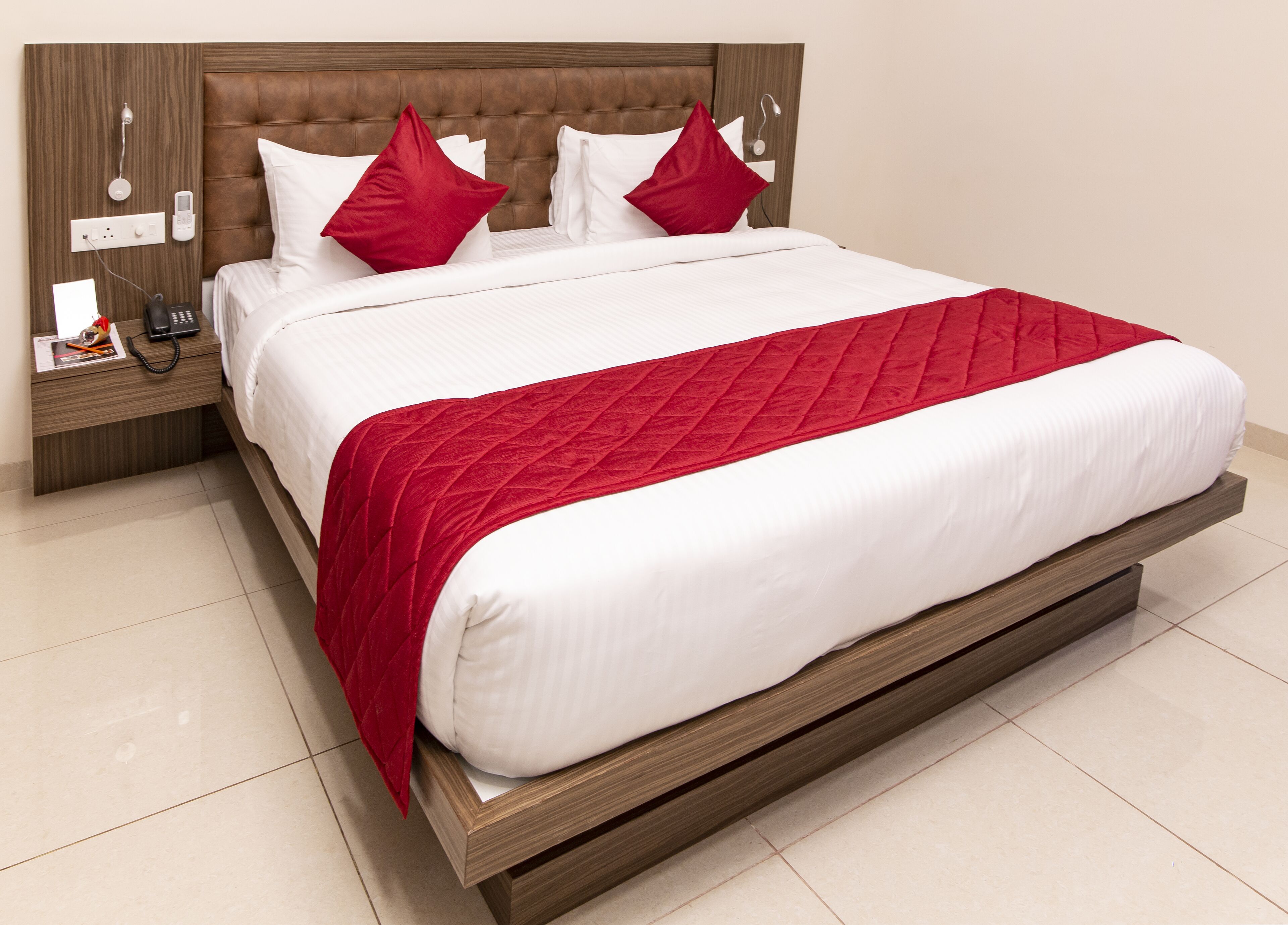 Una habitación de hotel moderna con una cama grande, cabecera de madera, mesita de noche con teléfono y una manta roja.