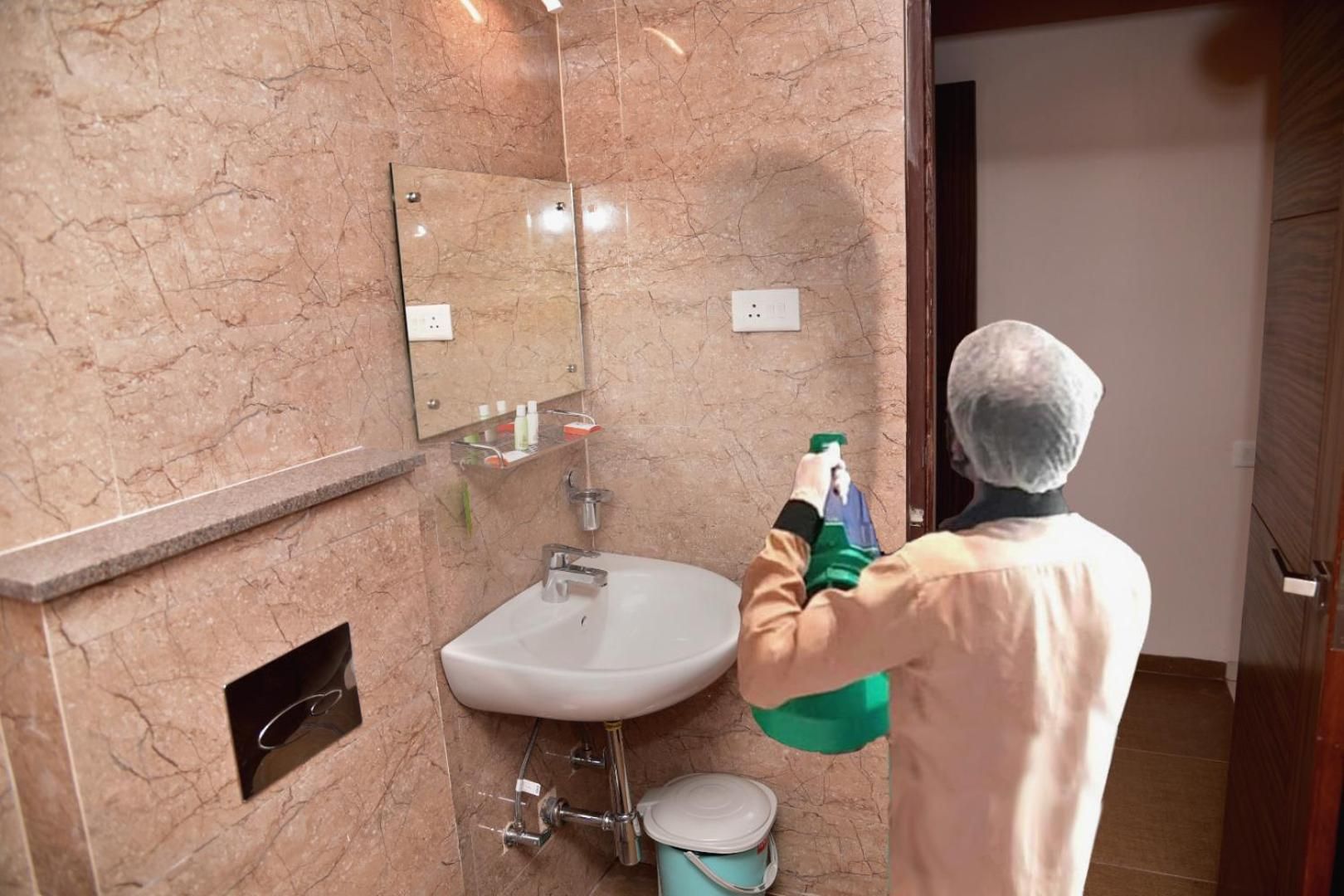 A bathroom with a sink, mirror, and a person spraying a cleaning product.