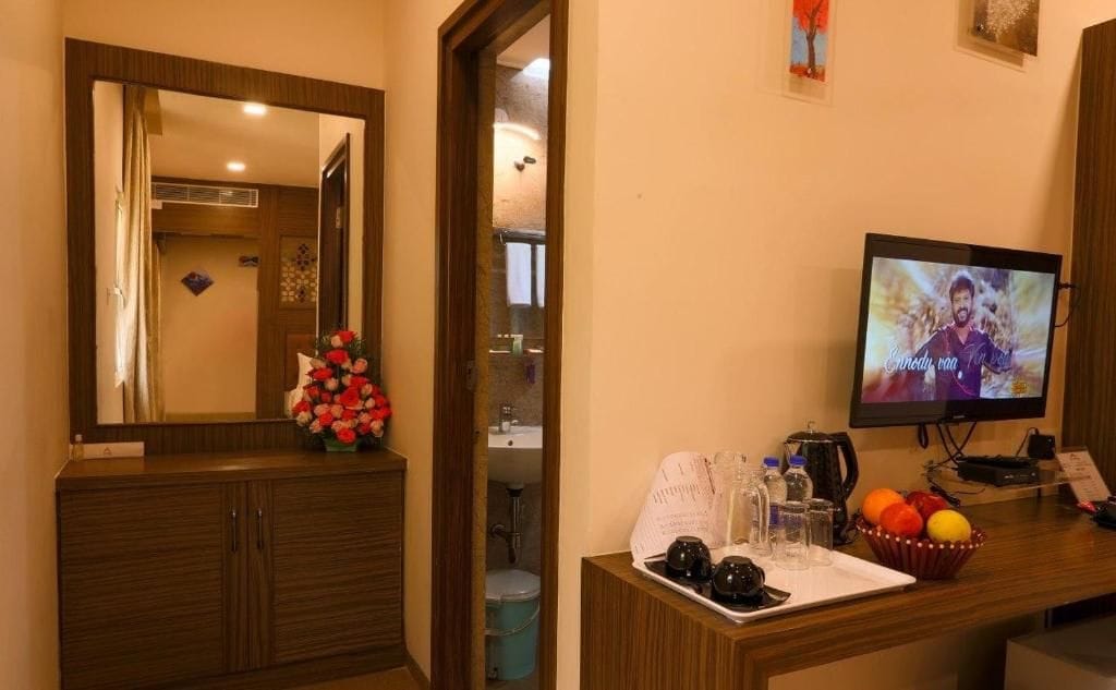 A hotel room with a wooden cabinet, a mirror, a television, a small table with a tray of items, and a wall-mounted picture.