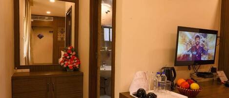 A hotel room with a wooden cabinet, a mirror, a television, a small table with a tray of items, and a wall-mounted picture.