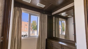 Una habitación con un ventanal grande, un armario de madera y un espejo.