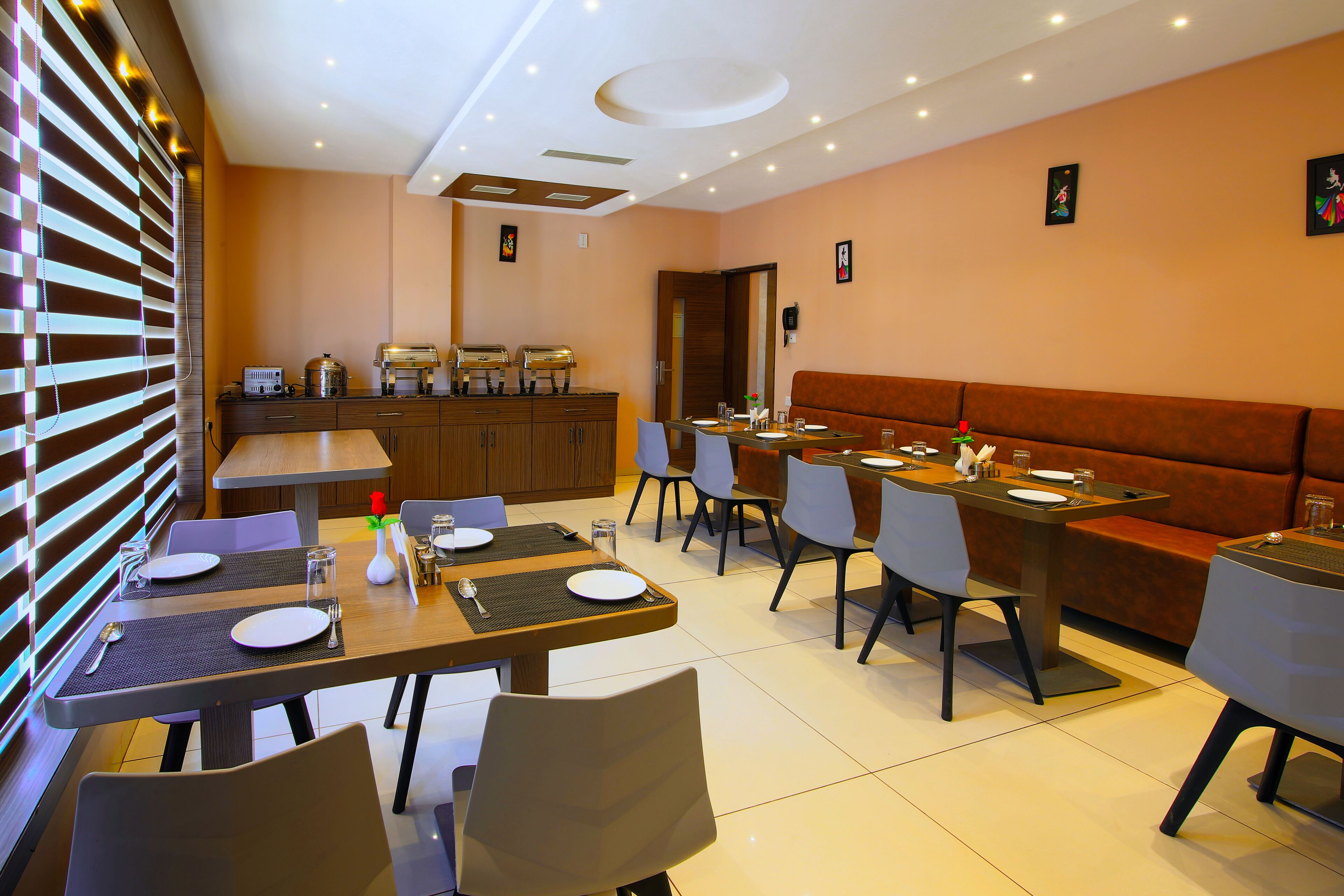 A modern dining area with tables set for four, a kitchen area with buffet service, and a seating area with a sofa.