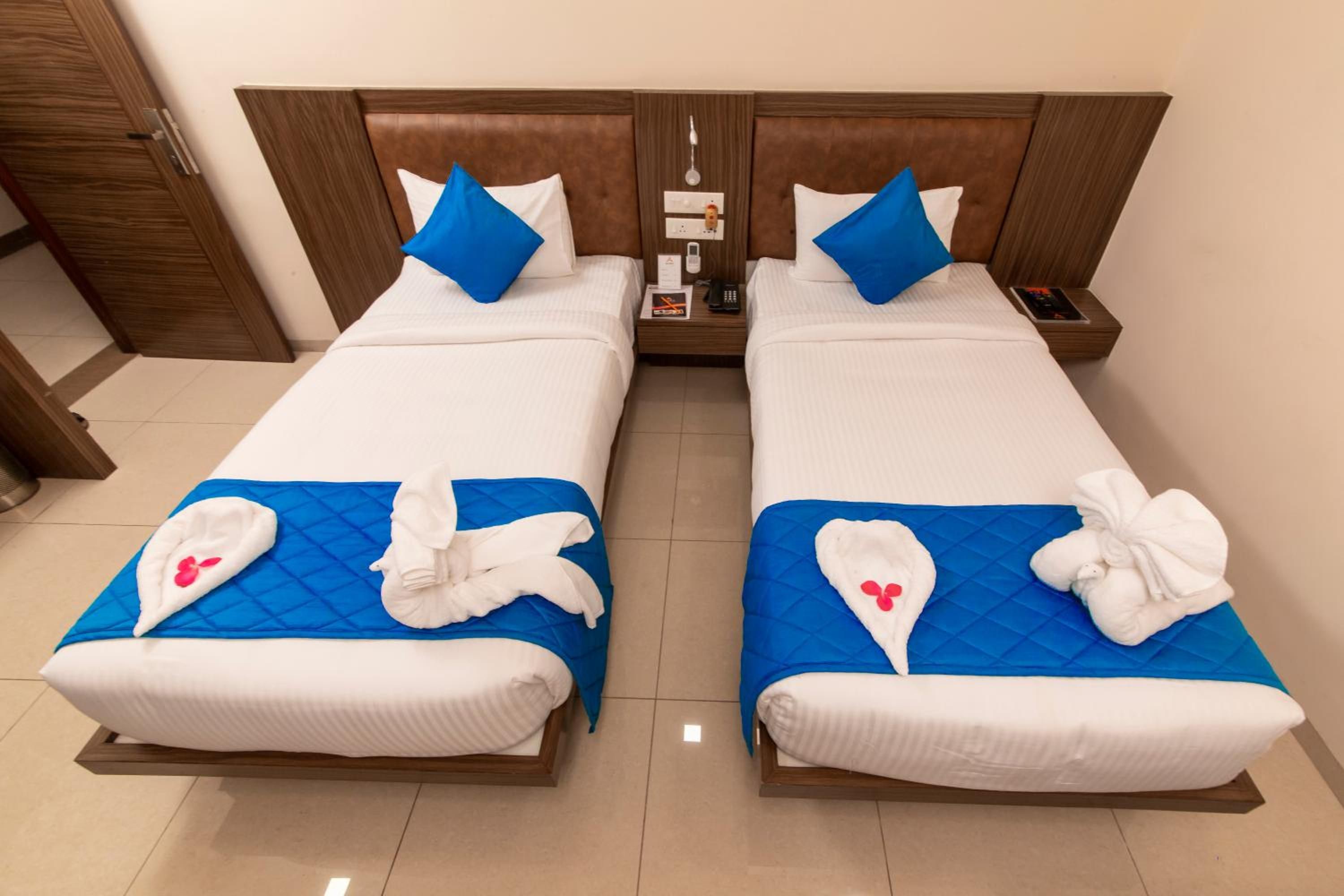 A hotel room with two beds, each with a blue quilted bedspread and white linens. There are towels with red flowers on the beds.