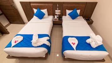 Habitación de hotel con dos camas, cada una con colcha azul acolchada y ropa blanca. Hay toallas con flores rojas sobre las camas.