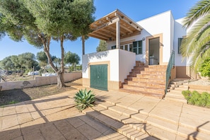 A modern house with a wooden pergola, a green door, and a staircase leading to the entrance. - APARTMENT WITH WIFI AND A/C, CLOSE TO BEACHES: SALMOINA COVE AND CALO DES MORO (Cala s'Almonia)