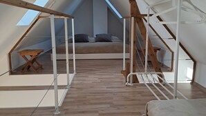 A spacious attic bedroom with a sloped ceiling, a skylight, a wooden table, a bed, and a staircase. - Exclusive & modern - right on the lake - spacious apartment with balcony (Wesenberg)