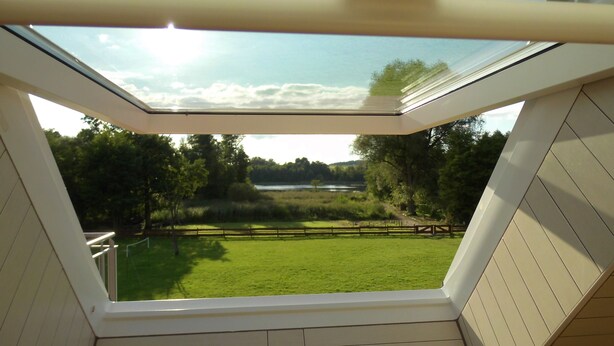 A skylight in a room with a view of a grassy area and trees. - Exclusive & modern - right on the lake - spacious apartment with balcony (Wesenberg)