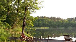 A lakeside setting with a wooden dock, two wooden chairs, and a barbecue grill. - Exclusive & modern - right on the lake - spacious apartment with balcony (Wesenberg)