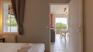 A hotel room with a bed, a window with curtains, a radiator, and a view of an outdoor balcony with a table and chairs.