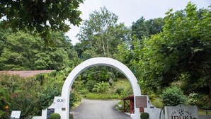 A white archway leading to a pathway surrounded by lush greenery and a sign with 'IDUKI' written on it.