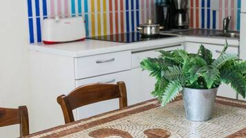Una cocina con encimera blanca, cafetera, tostadora y un helecho en una mesa de mosaicos.