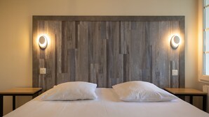 A double bed with white linens, two bedside tables, and a wooden headboard with wall-mounted lighting.
