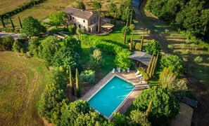 An aerial view of a property with a swimming pool, a stone house, and surrounding greenery.
