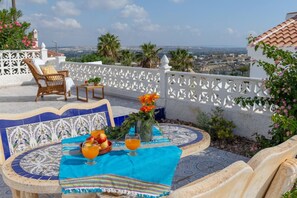 A terrace with a table set for two, a wicker chair, and a view of the cityscape. - Fidalsa Golf & Beach (Ciudad Quesada)