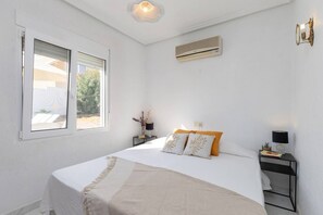 A bedroom with a bed, bedside tables, an air conditioning unit, and a window. - Fidalsa Golf & Beach (Ciudad Quesada)