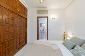 Une chambre à coucher comprenant un lit, une table de chevet, une lampe fixée au mur et une armoire en bois.
