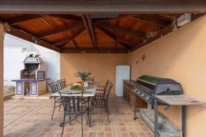 An outdoor patio with a table, chairs, a grill, and a refrigerator.