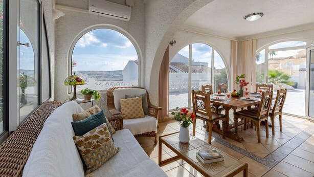 Ein großzügiger Wohnbereich mit Sofa, Esstisch und Stühlen, großen Bogenfenstern und Blick auf die Stadt.