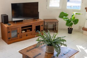 A wooden entertainment unit with a flat-screen TV, speakers, and storage drawers. A woven plant pot is on a wooden table in the foreground. - Fidalsa Golf & Beach (Ciudad Quesada)