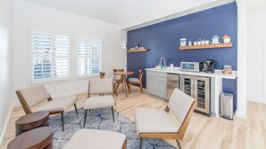 Una cocina moderna con una pared azul de acento, armarios de madera y un microondas integrado. En la zona de estar hay dos sillas y una mesa redonda pequeña.