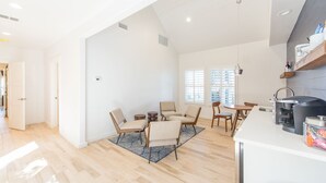 Amplia sala de estar con una mesa de comedor, varias sillas y una zona de cocina con cafetera.