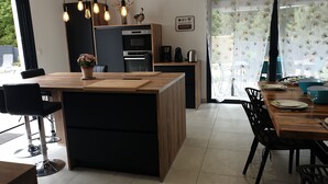 A modern kitchen with a central island, wooden cabinetry, and pendant lighting. - Villa palm grove-private pool and bowling green (Saint-Jean-de-Monts)