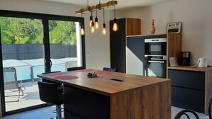 A modern kitchen with a wooden island, built-in appliances, and a view of the backyard. - Villa palm grove-private pool and bowling green (Saint-Jean-de-Monts)