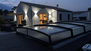 A modern house with a covered outdoor area featuring a glass enclosure, a patio with outdoor furniture, and a satellite dish on the roof. - Villa palm grove-private pool and bowling green (Saint-Jean-de-Monts)