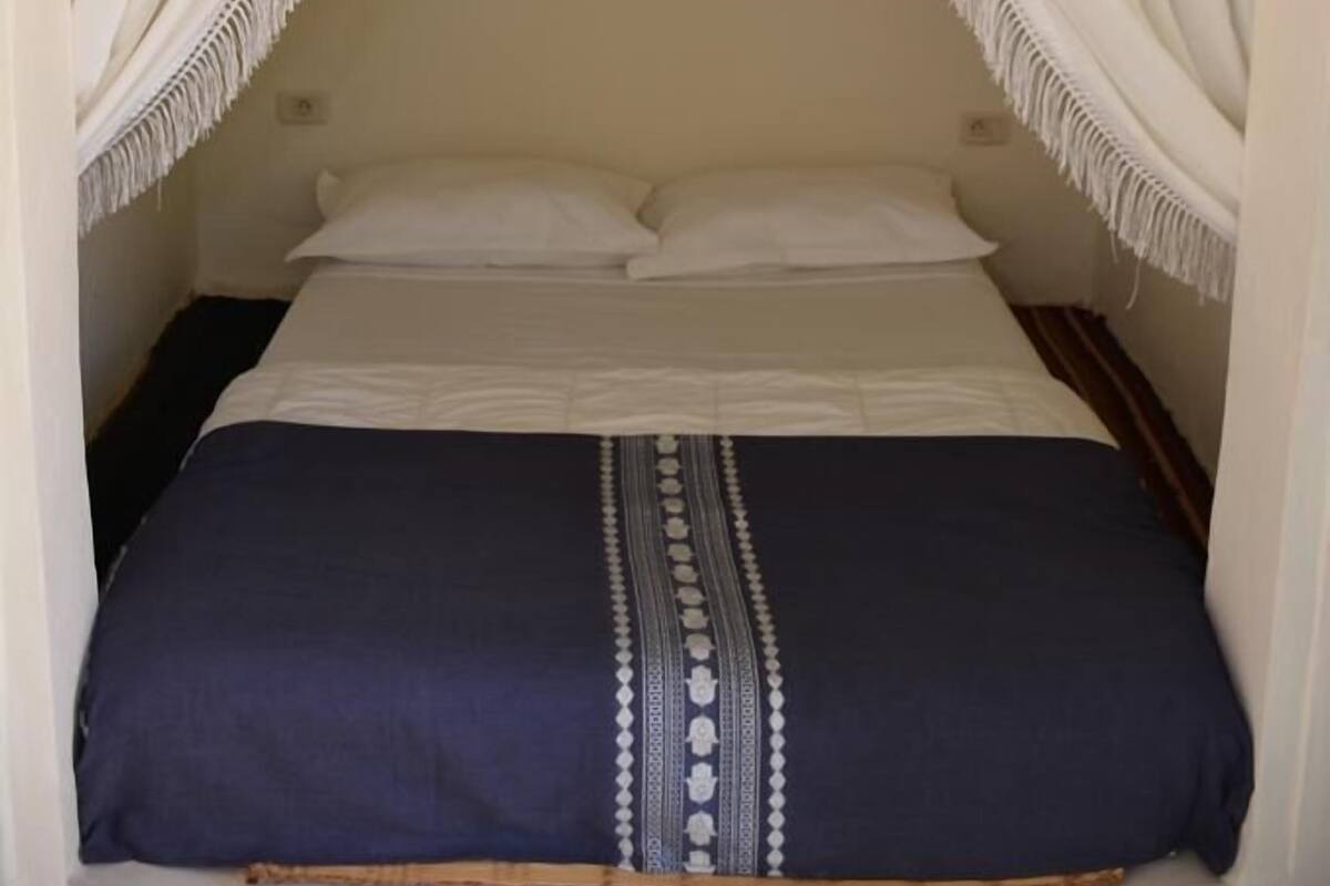 A bed with a canopy, a painting on the wall, and a patterned bedspread.