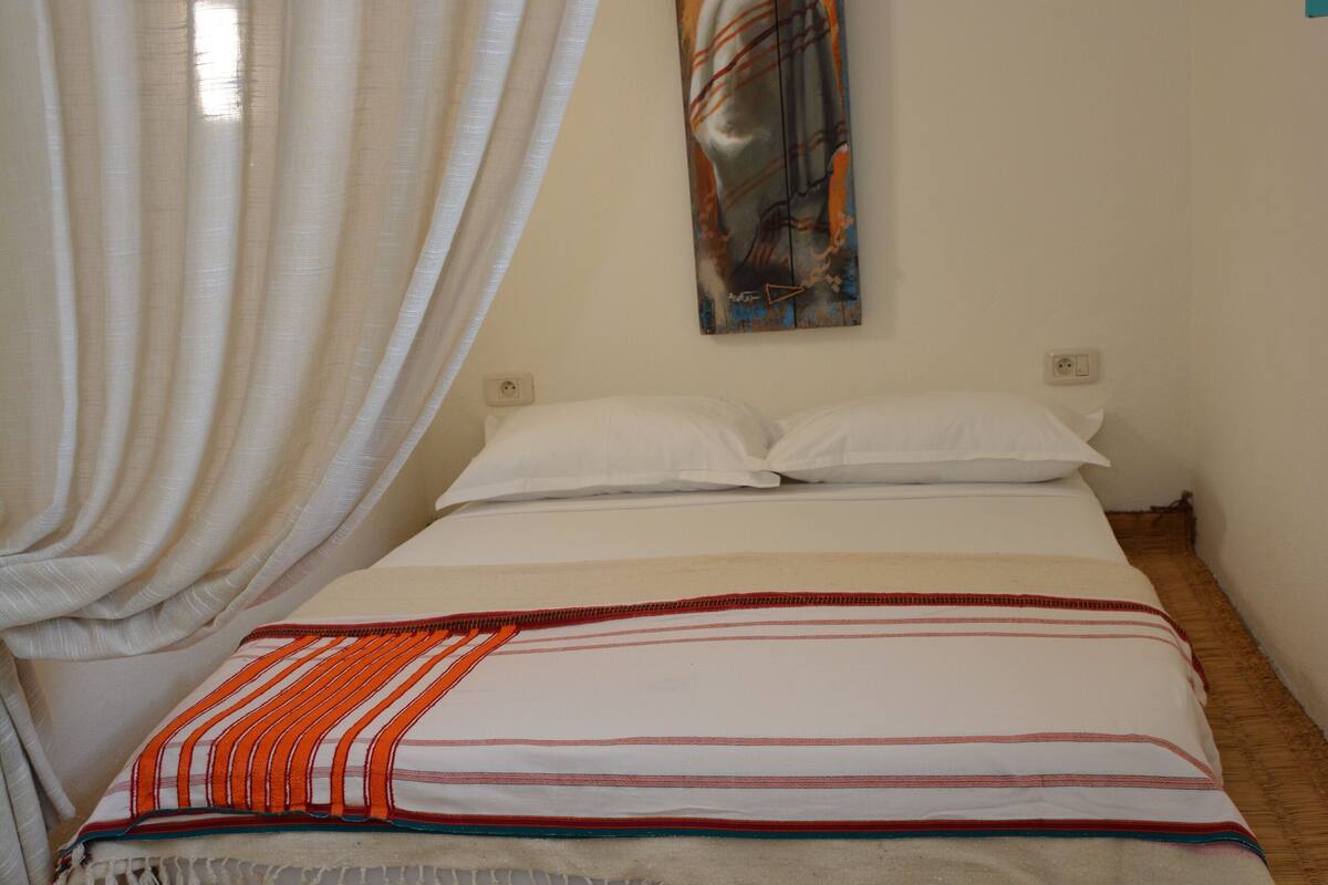 A bedroom with a bed, a painting, a curtain, and a fur rug.