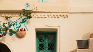 A set of beige stone steps leading to a door with a green decorative grille. - Dar Lily (Erriadh)