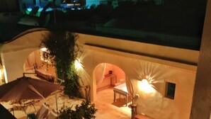 A rooftop terrace with a seating area, potted plants, and a view of the cityscape at night. - Dar Lily (Erriadh)