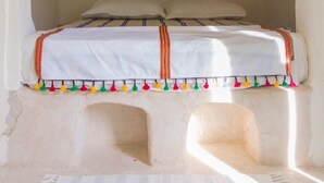 A bed with a canopy, a painting on the wall, and a stone bench. - Dar Lily (Erriadh)