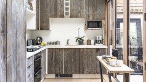 A compact kitchen with wooden cabinetry, a microwave, and a small dining area with a table and chairs. - Retreat to a Stylish Flat in Chelsea (London)