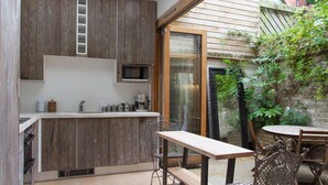 A compact kitchen with wooden cabinets, a built-in microwave, and a small dining area with a table and chairs. - Retreat to a Stylish Flat in Chelsea (London)