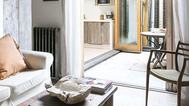 A cozy living room with a white sofa, a coffee table with a bowl and magazines, and a view of the outside patio area. - Retreat to a Stylish Flat in Chelsea (London)