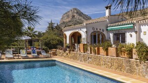 A pool area with lounge chairs and a stone wall. - La Golondrina (Javea / Xàbia)