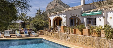 A pool area with lounge chairs and a stone wall.