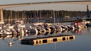 Un puerto deportivo con numerosas embarcaciones amarradas, un puente al fondo y agua tranquila que refleja las barcas.