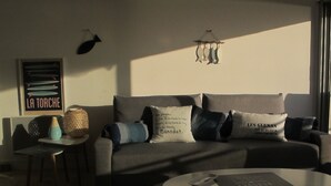 Una sala de estar moderna con un sofá, una mesita de centro y una pequeña mesa con un florero. Hay un cartel en la pared y una lámpara colgante.