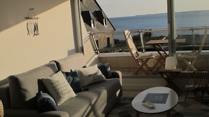 Un salón moderno con un sofá, una mesita redonda y vista al mar.