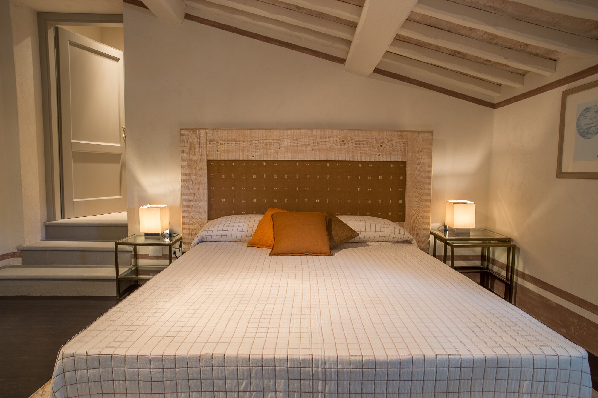 A hotel room with a large bed, a headboard with a patterned design, two bedside lamps, and a framed picture on the wall.